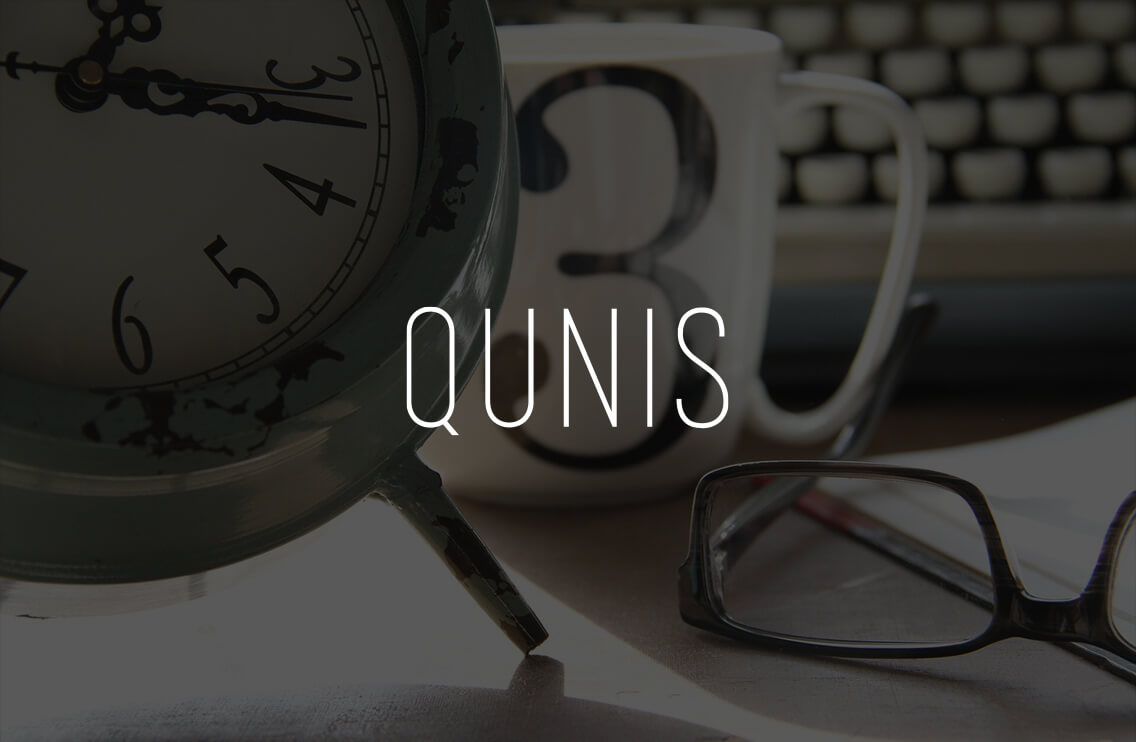 Desk with analog clock, glasses and coffee cup in front of a keyboard, with the lettering 